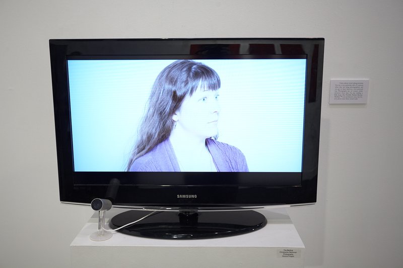 An art display with a portrait on an LCD screen with a webcam. The portrait is looking off to the right.